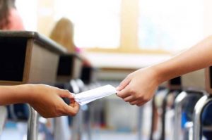 Cropped image of two school kids handing notes to each other secretly during class